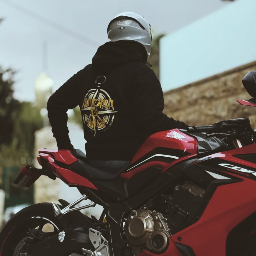 Person from behind on a red sport motorcycle wearing a black hoodie with gold graphic artwork